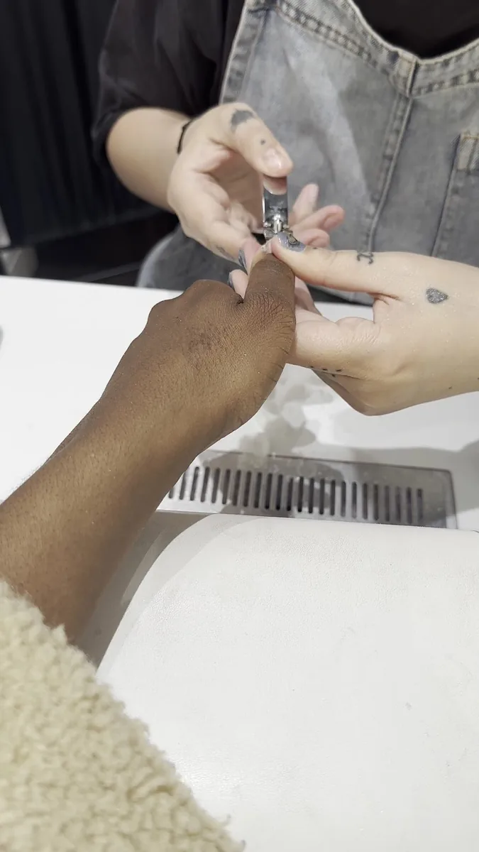 A nail technician painting a client's nail at the manicure desk, both pairs of hands close in frame.