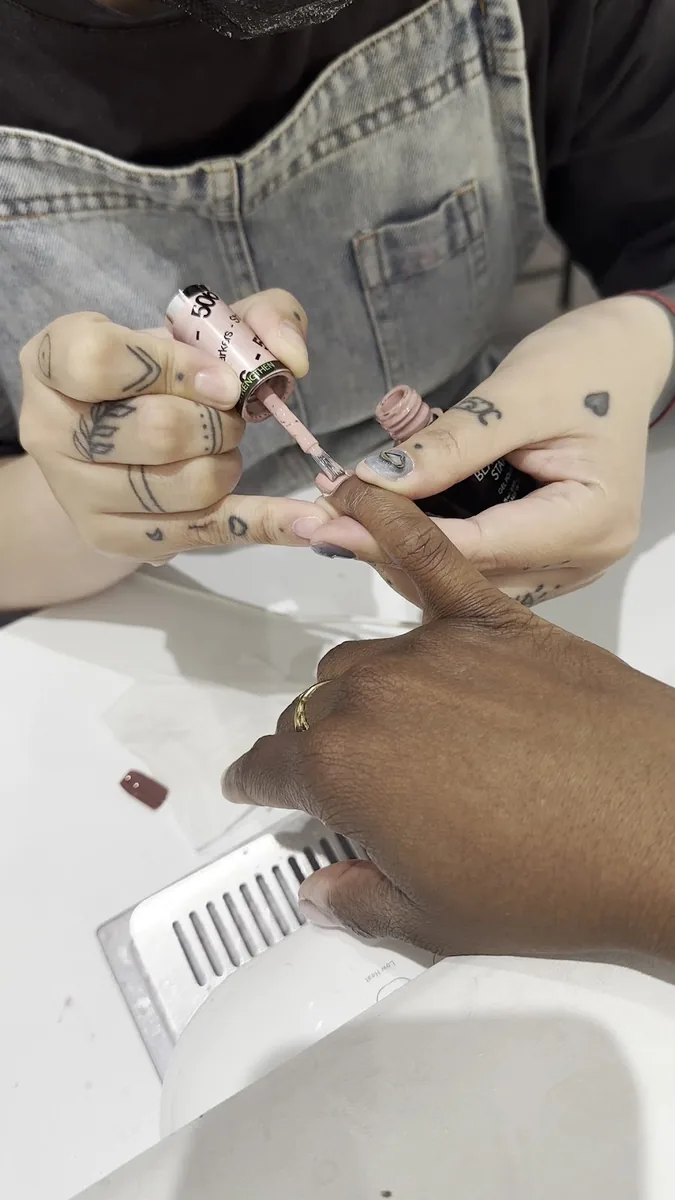 Close-up of a technician applying polish to a client's finger resting over a nail file on the table.
